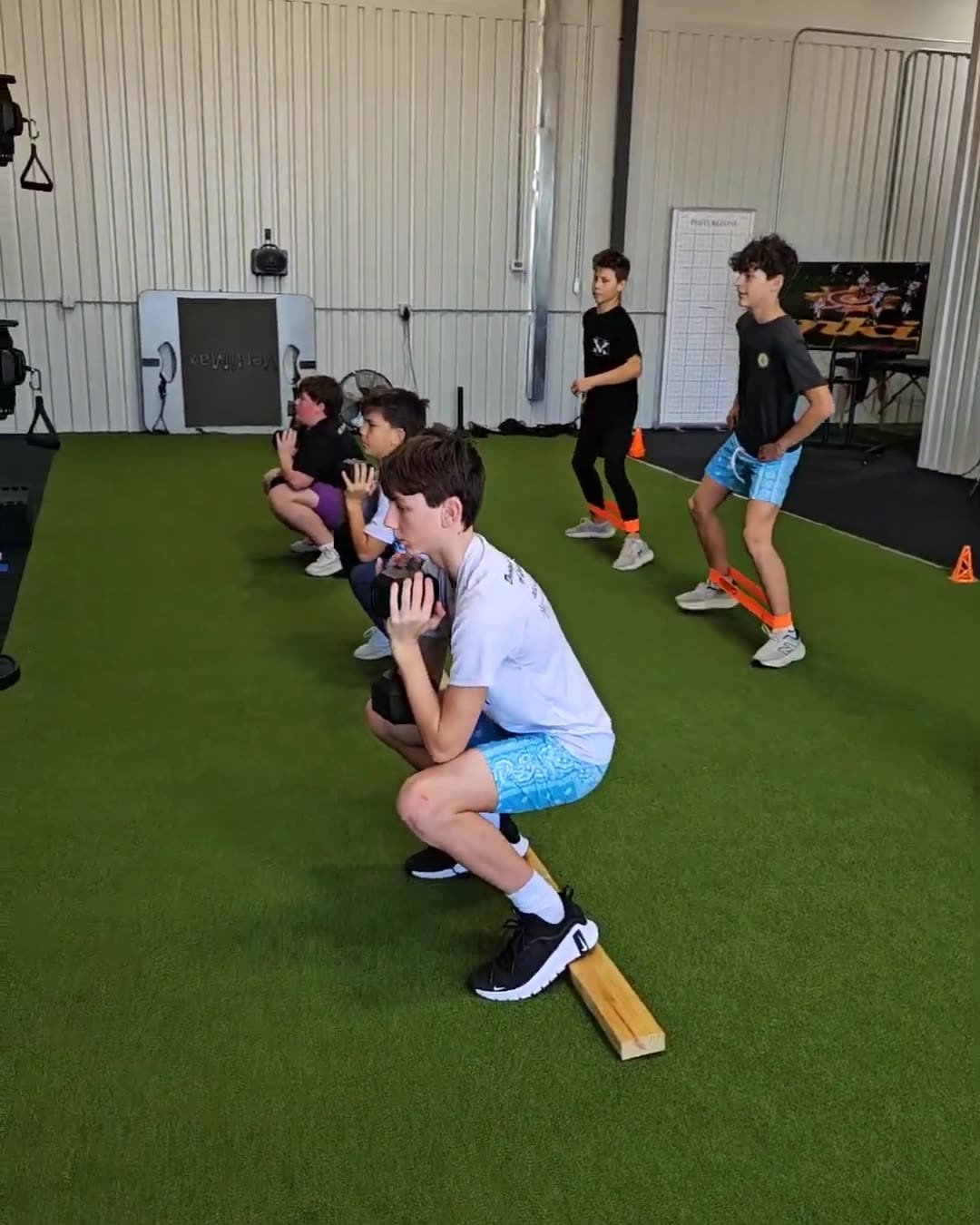 Youth athletes training together at Activ8: goblet squats and banded lateral walks